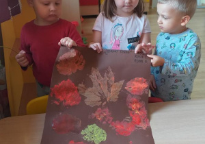 Adaś, Zosia i Miłosz prezentują wykonany przez siebie "jesienny dywan".